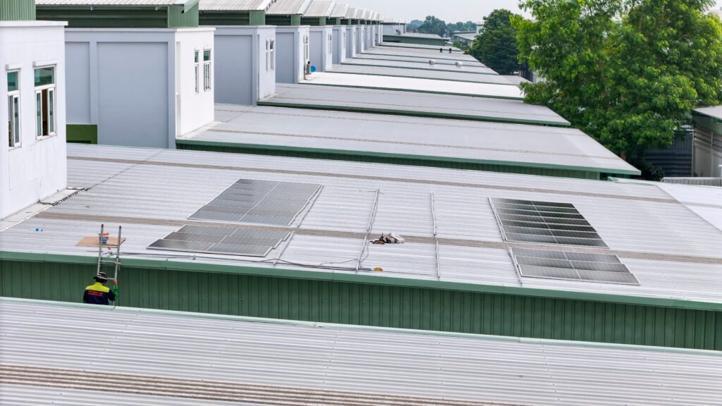 Technicien en équipement de sécurité inspectant des panneaux solaires sur un toit métallique.